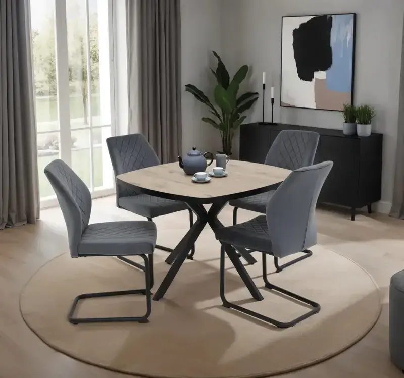 Esszimmer mit rundem Holz Esstisch auf schwarzem Kreuzgestell, vier grauen Polsterstühlen auf rundem Teppich, hinten Sideboard, Pflanze und Fenster mit Vorhängen.